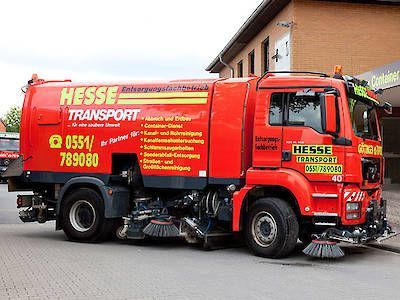 Ein roter Lastwagen mit gelber Aufschrift parkt auf einer Straße neben einem Gebäude.