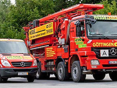 Rotes Feuerwehrauto und Rettungswagen auf einer Straße, mit deutschem Text und einer von Bäumen gesäumten Kulisse