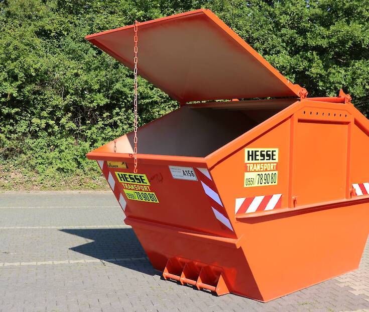 Ein orangefarbener HESSE-Abfallcontainer mit offenem Deckel steht am Straßenrand, dahinter grüne Bäume.