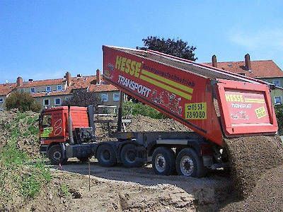 Ein roter Muldenkipper lädt Kies an einer Straßenbaustelle unter blauem Himmel ab