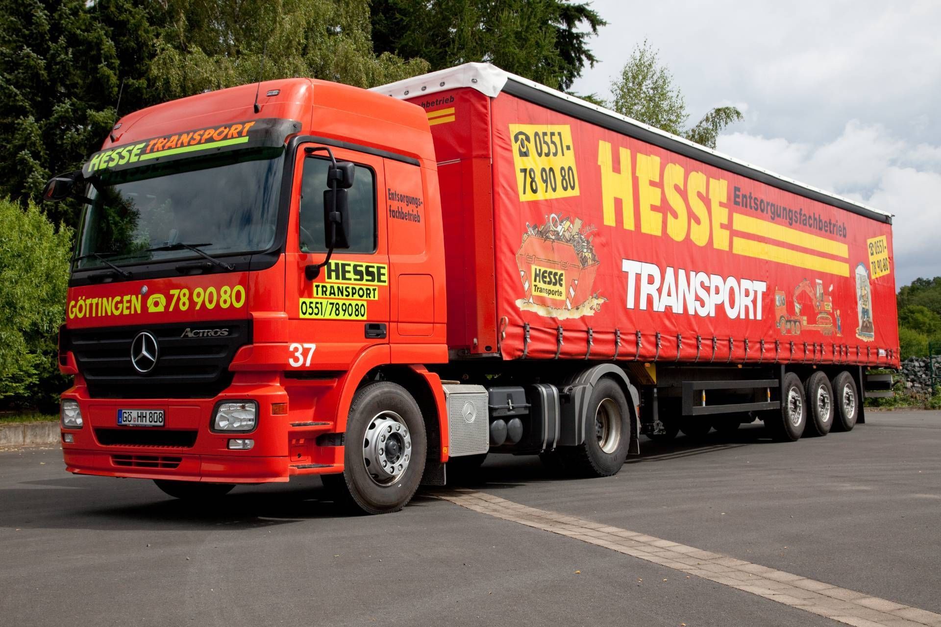 Ein roter Sattelzug von HESS Transport parkt auf einer Straße mit Bäumen im Hintergrund.