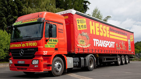 Ein roter Sattelzug der Firma HESS Transport mit rotem Anhänger parkt am Straßenrand.