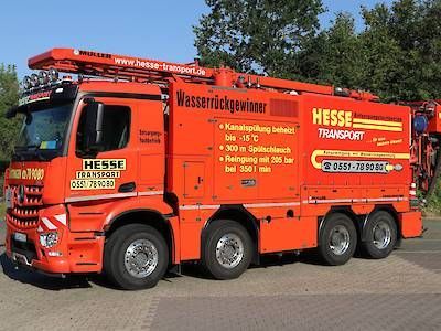 Ein leuchtend orangefarbener Wassertankwagen der Firma Hesse Transporter parkt im Freien unter blauem Himmel.