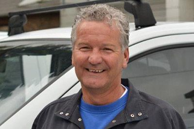 Ein Mann in einem blauen Hemd lächelt vor einem weißen Lieferwagen.