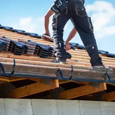 Trabajadores de la construcción instalan tejas de arcilla en el tejado de una casa bajo un cielo azul.