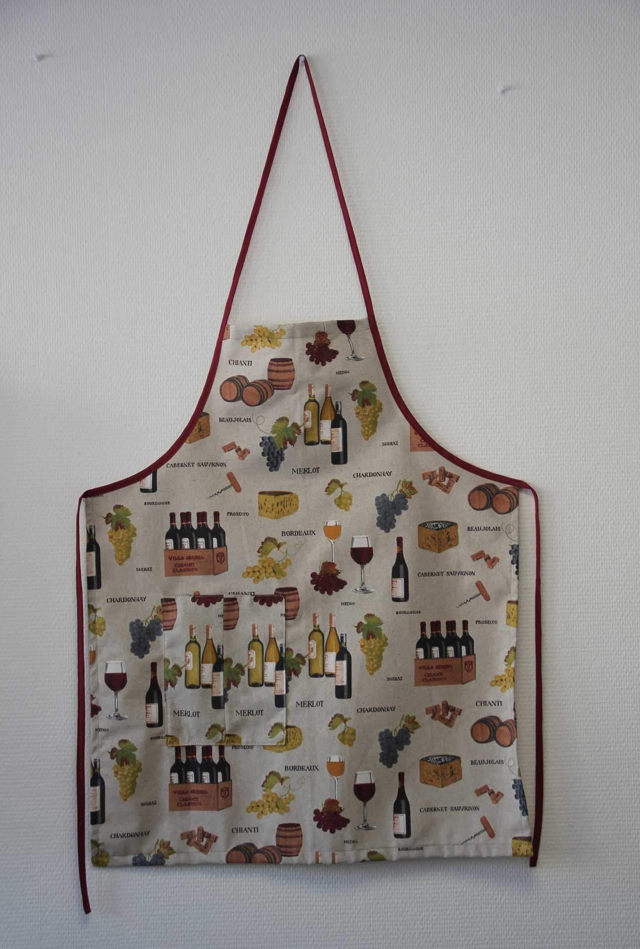 Tablier de cuisine à motifs avec une lanière rouge autour du cou et un corps blanc, suspendu sur un fond uni