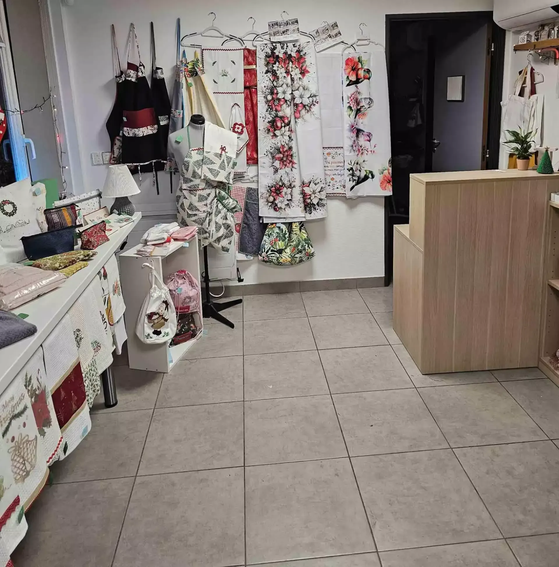 Intérieur d'une petite boutique avec des étagères de vêtements et de décorations florales, et un comptoir en bois au premier plan.