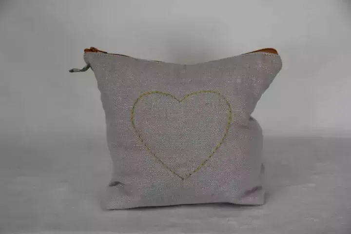 Petit coussin gris avec un contour de cœur brodé et des languettes marron aux coins sur fond blanc