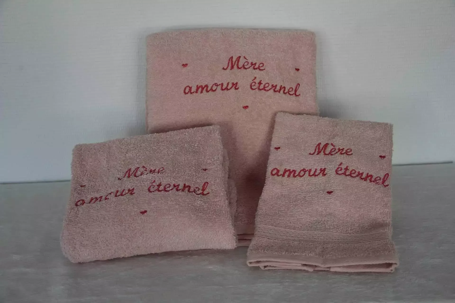 Trois serviettes roses brodées de l'inscription « Mon amour éternel » sur fond clair