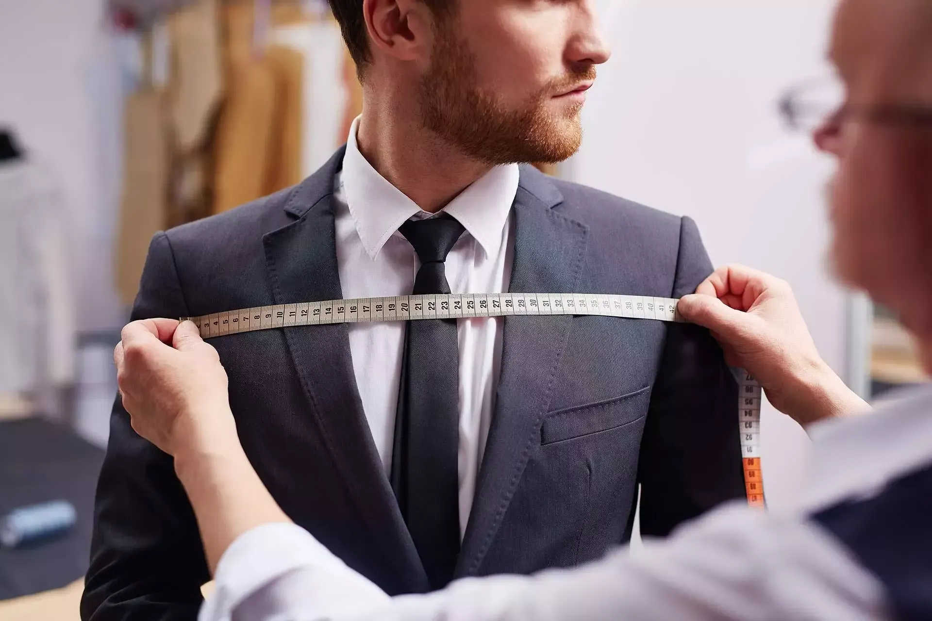 Un tailleur prend les mesures d'une veste de costume pour homme avec un mètre ruban dans une cabine d'essayage