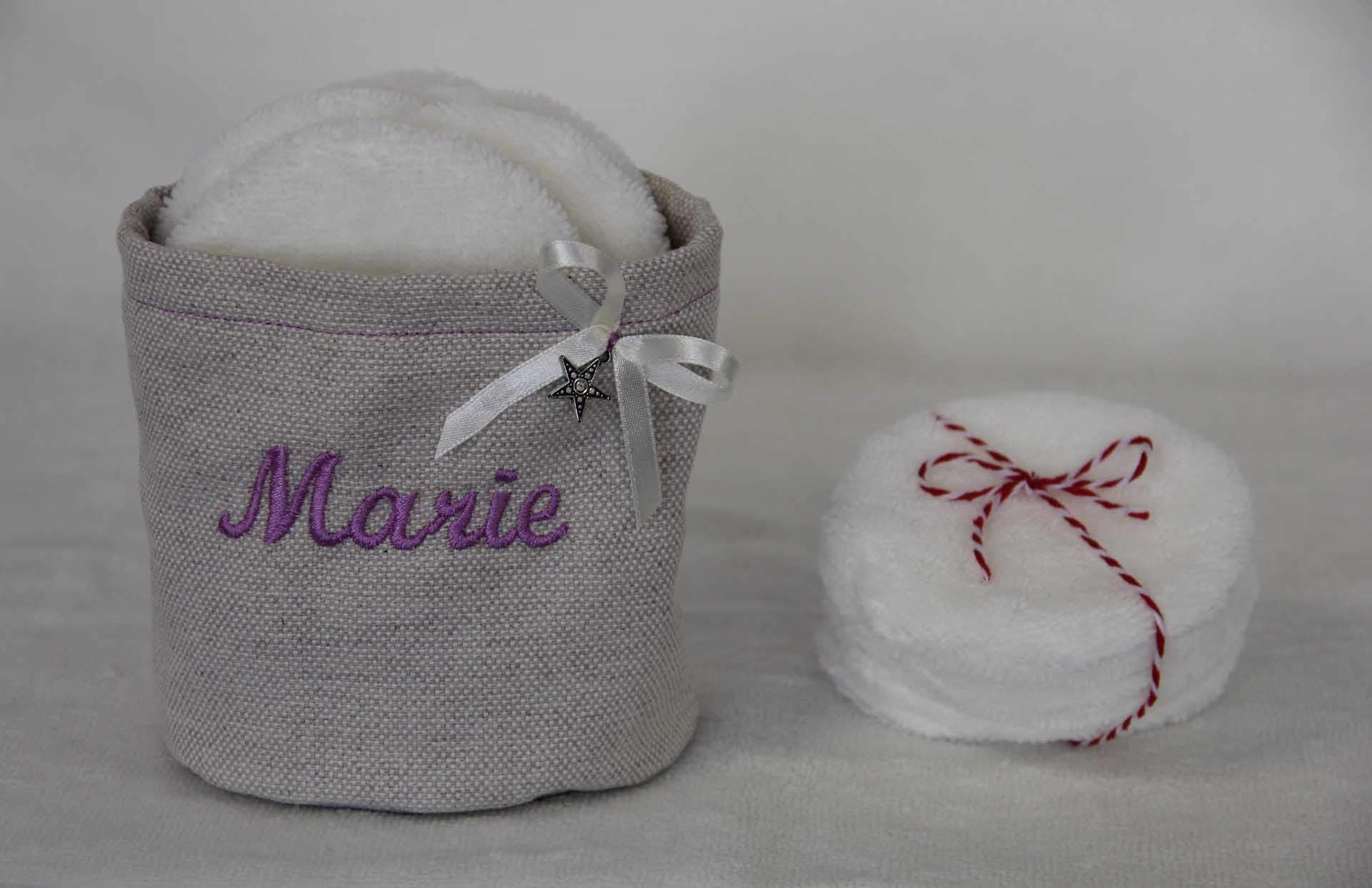 Deux articles de bain blancs : un panier gris étiqueté « Marie » et un paquet rond noué avec une ficelle rouge.