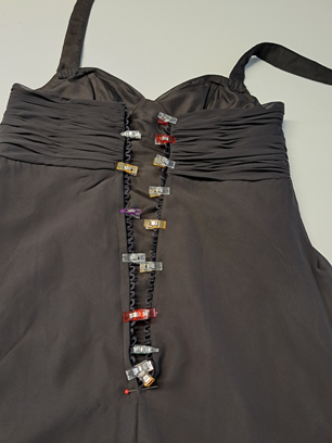 Robe noire à lacets latéraux et clips multicolores au centre, sur fond blanc.