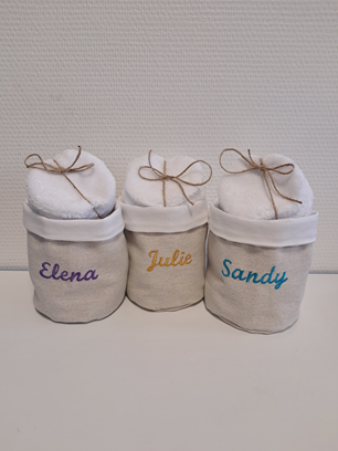 Trois sacs cadeaux blancs personnalisés, étiquetés Elena, Julie et Sandy, avec des rubans noués sur un fond neutre.