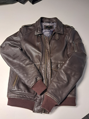 Blouson aviateur en cuir marron avec poignets et ourlet côtelés, posé à plat sur une surface claire.