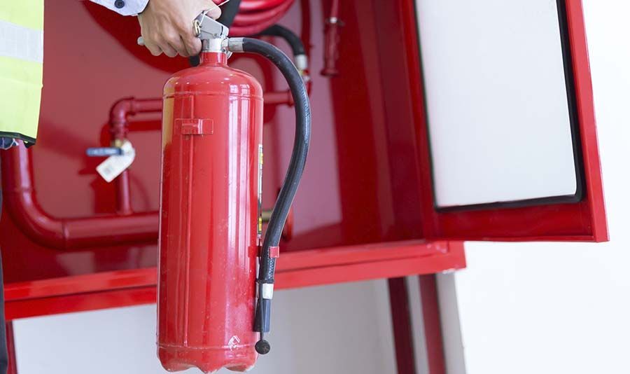 Un hombre sostiene un extintor rojo frente a una boca de incendios roja.