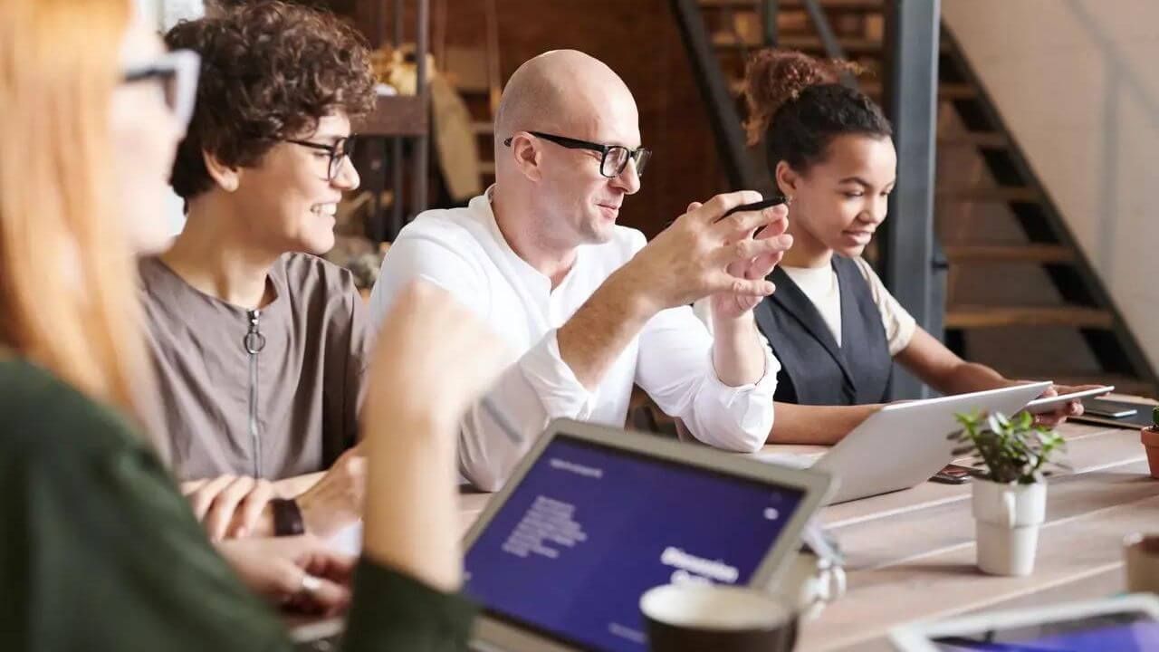 A group of people are sitting around a table with laptops.