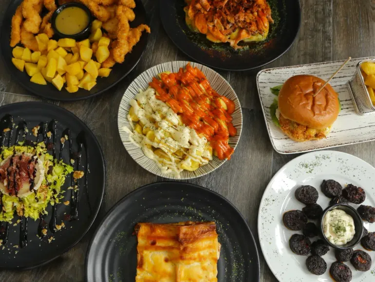 Toma aérea de varios platos: pasta, hamburguesas, patatas fritas, tiras de pollo y otros platos servidos.