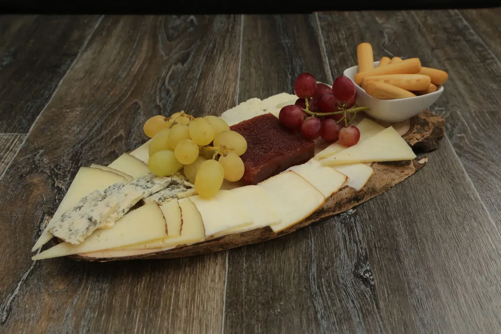 Plato de quesos y uvas con palitos de pan sobre una superficie de madera.