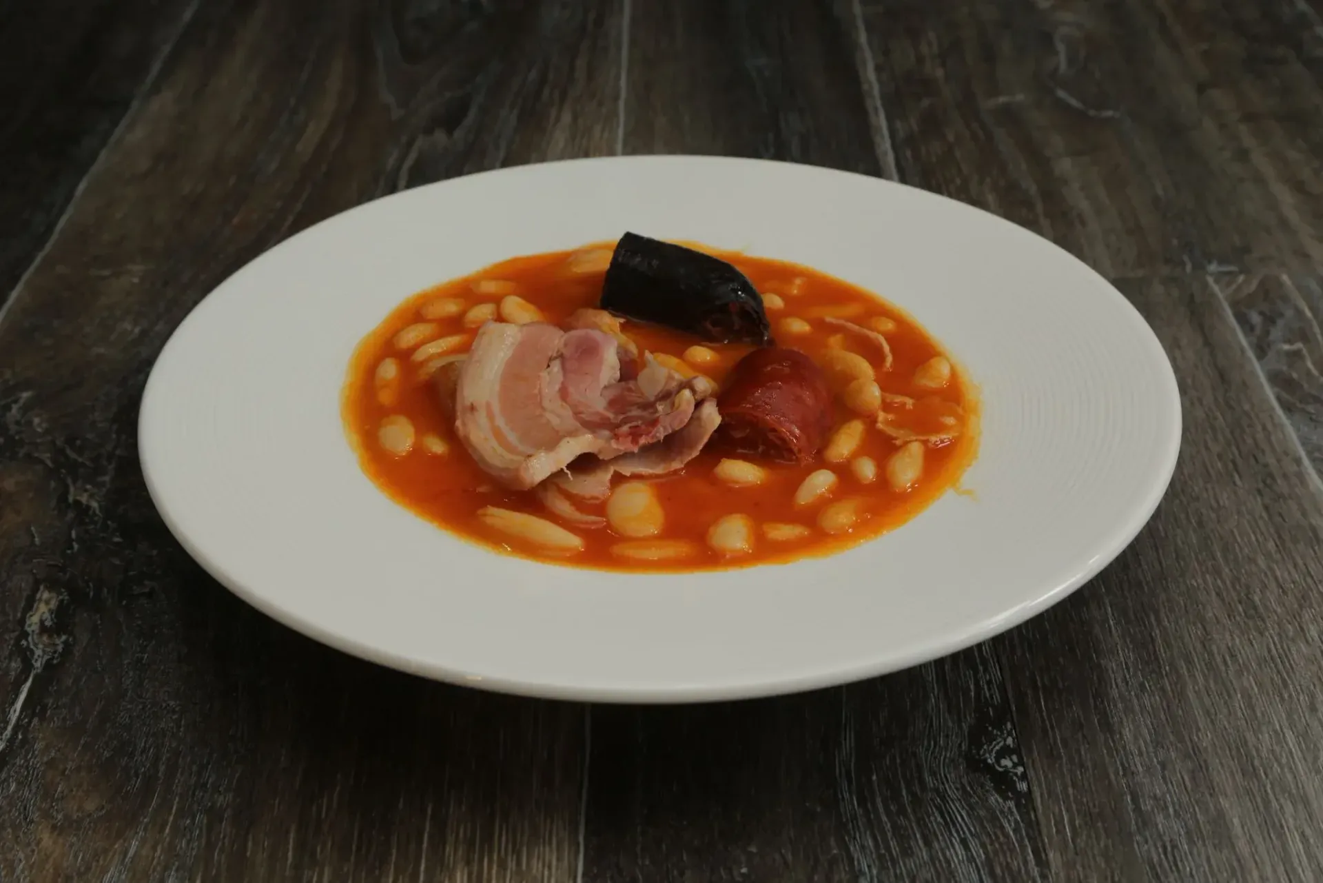 Alubias blancas en salsa de tomate con carne en un plato blanco.