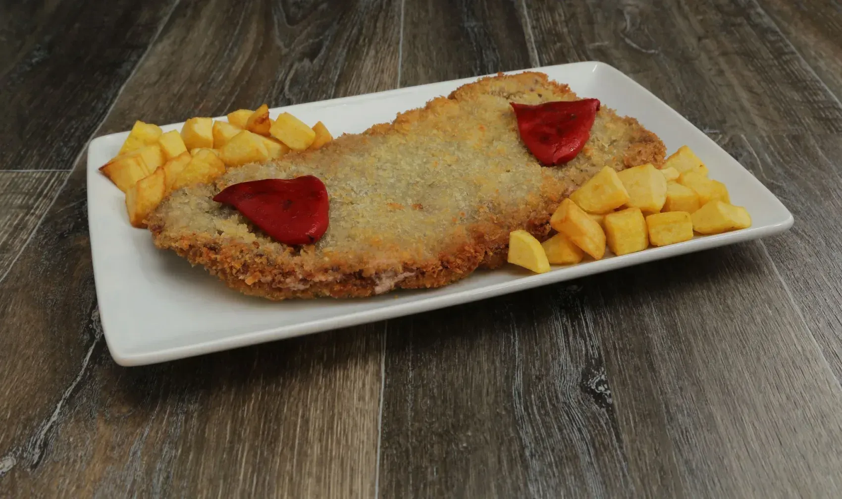 Milanesa de carne con pimiento rojo y patatas fritas en un plato blanco.