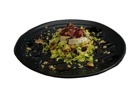 Ensalada con queso de cabra, nueces y glaseado balsámico en un plato negro.