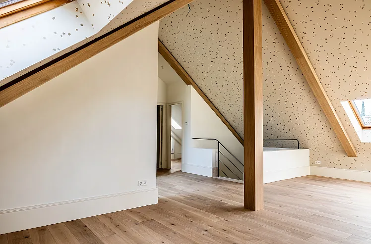 Un ático vacío con vigas de madera y una escalera.