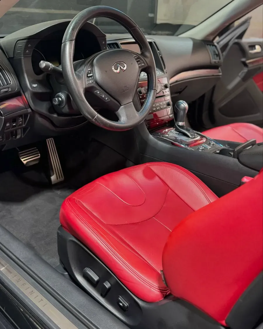 Interior del coche con asientos de cuero rojo, volante y consola central con palanca de cambios y controles.