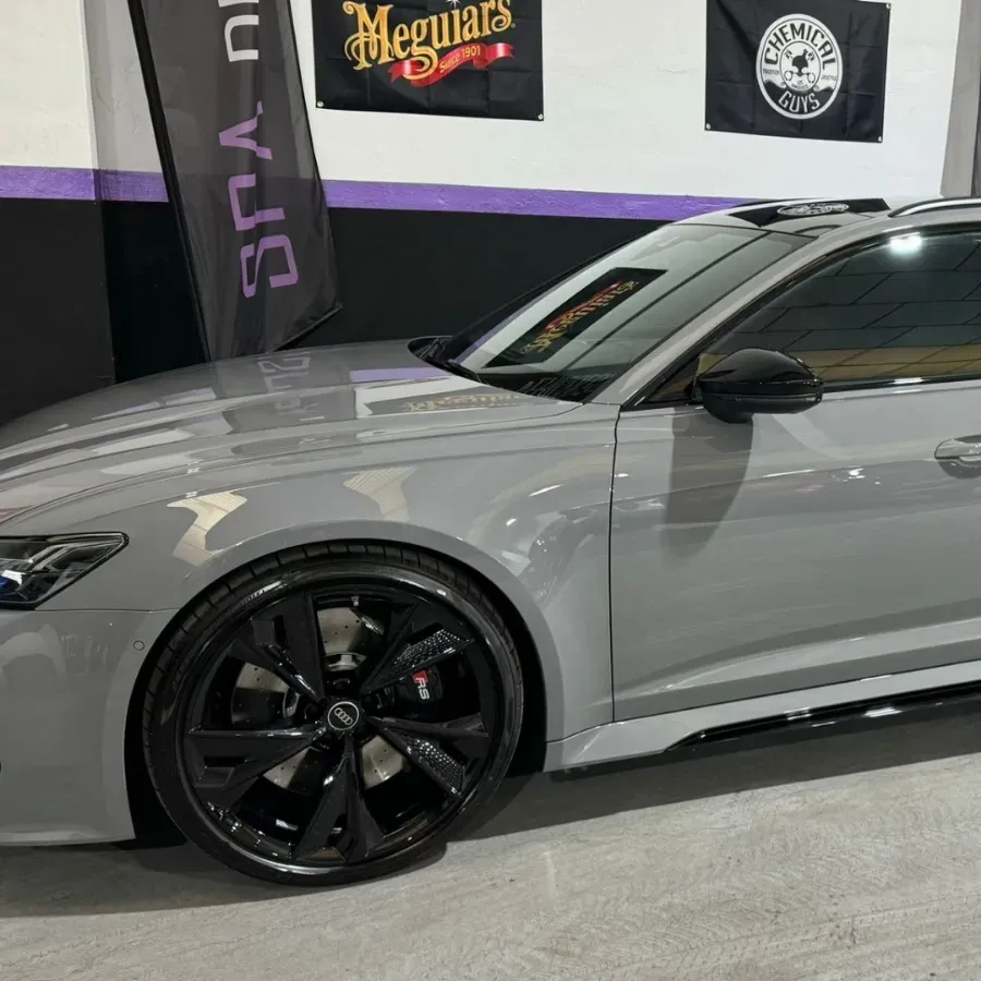 Sedán gris con llantas negras estacionado en el interior de un garaje con letrero de Meguiar's.