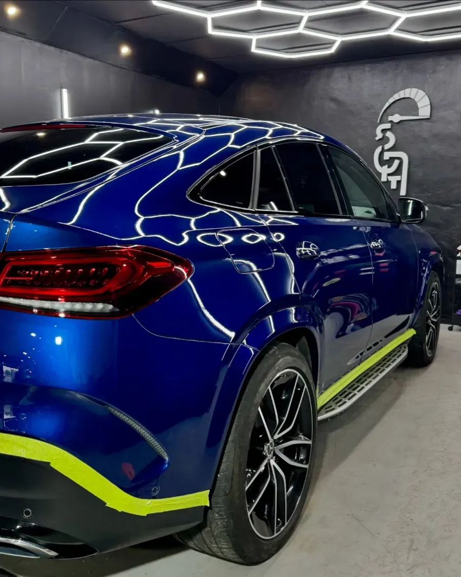 SUV deportivo azul con detalles en amarillo neón estacionado en el interior bajo luces de techo geométricas.