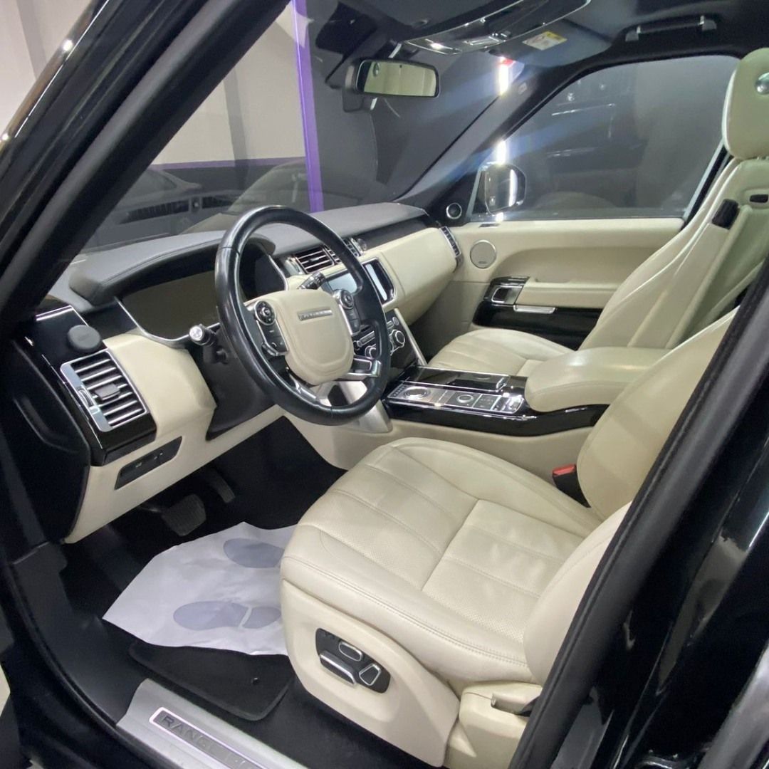 Interior de coche de lujo en cuero beige con puerta del conductor abierta y volante negro.