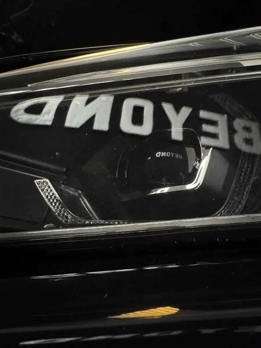 Texto “BEYOND” reflejado en la superficie oscura de un coche por la noche.
