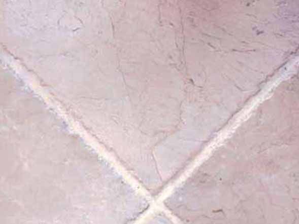 Un primer plano de un piso de baldosas rosas con lechada blanca.