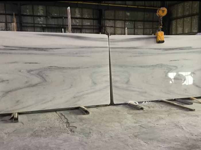 Una gran losa de mármol blanco reposa sobre un piso de concreto en un almacén.