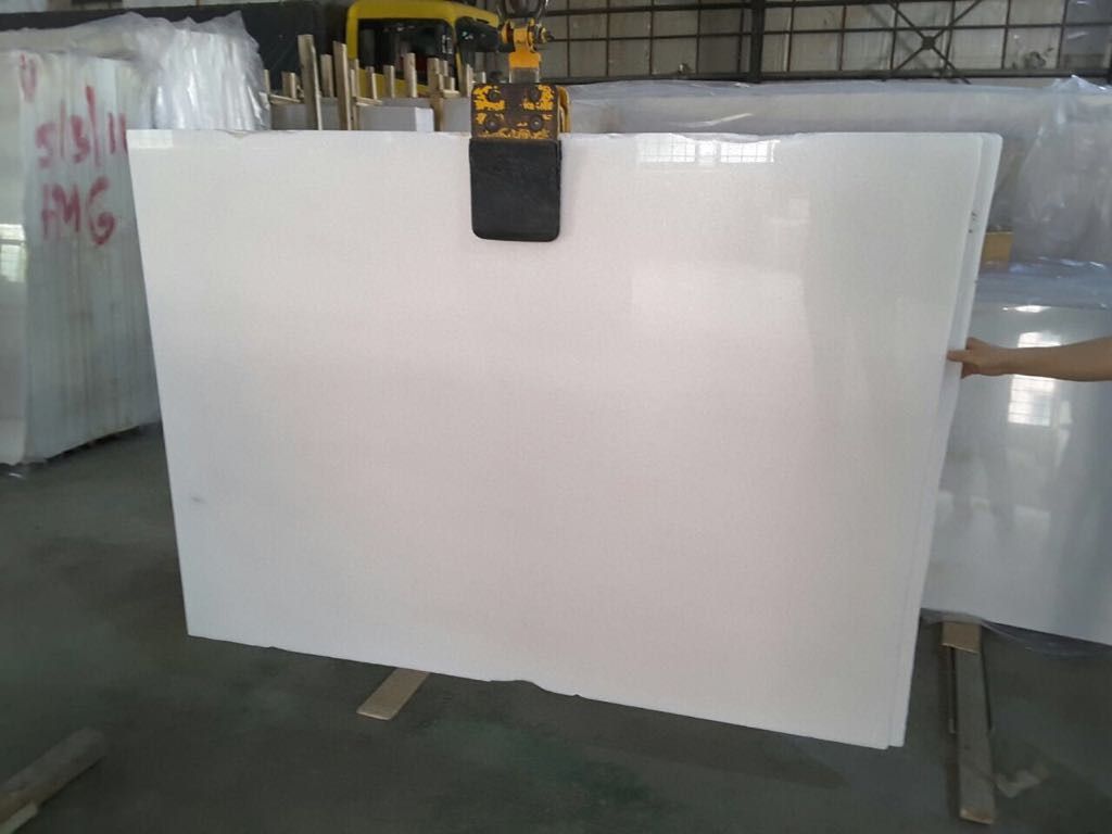 Una losa de mármol blanco está siendo levantada por una grúa en un almacén.