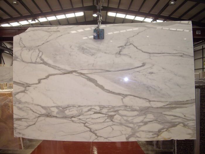 Una gran losa de mármol blanco cuelga de una grúa en un almacén.
