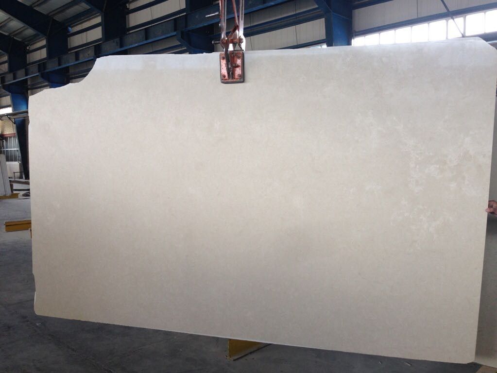 Una gran losa de mármol blanco cuelga de una grúa en un almacén.