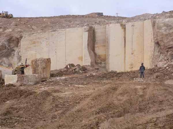 Un hombre está parado frente a un gran muro de piedra en una cantera.