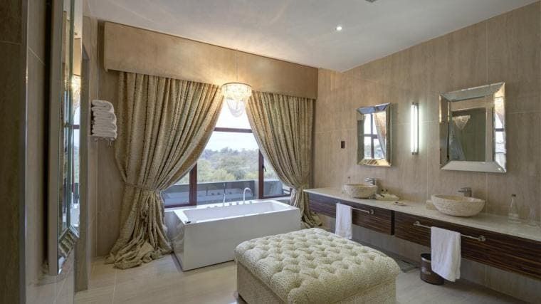 Un baño con bañera, lavabos, espejos y cortinas.