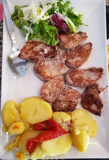 Carne a la parrilla, patatas y ensalada en un plato blanco.