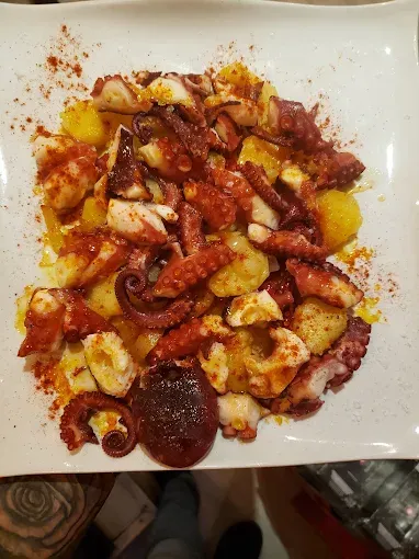 Plato de pulpo con patatas, aderezado con pimentón, en plato blanco.
