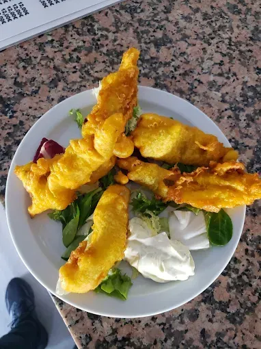 Pescado frito en un plato blanco con lechuga y una cucharada de salsa blanca sobre una encimera.