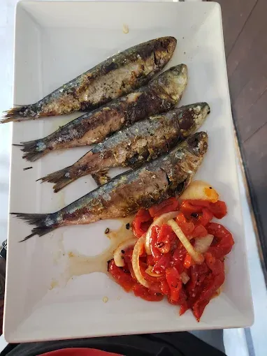 Sardinas a la parrilla con pimientos rojos y cebollas en un plato rectangular blanco.