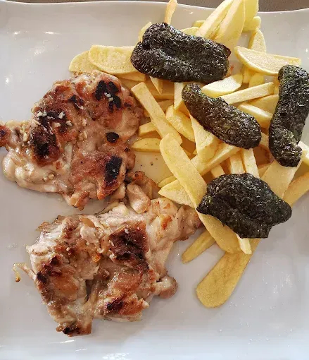 Pollo a la parrilla, papas fritas y pimientos verdes fritos en un plato blanco.