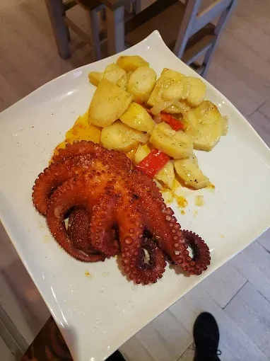 Pulpo a la plancha con patatas y pimientos rojos en plato blanco.