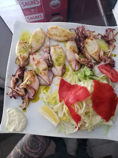 Calamares a la plancha con ensalada, pimientos rojos, limón y una cucharada de salsa en un plato blanco.