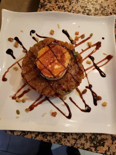 Pila de comida frita con una cubierta circular de color marrón dorado, rociada con salsa oscura y espolvoreada con nueces