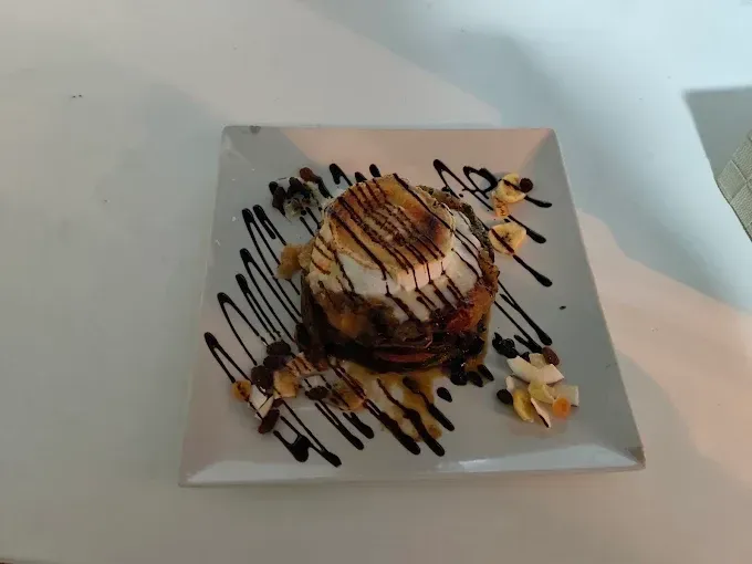 Postre en plato blanco: salsa de chocolate rociada, cobertura de malvavisco tostado y nueces.