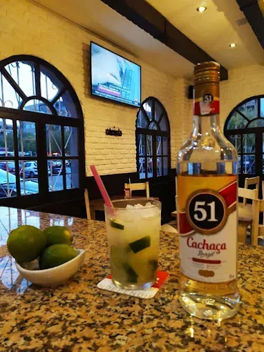 Cóctel de caipirinha con botella de cachaça en una barra; limas en un bol.