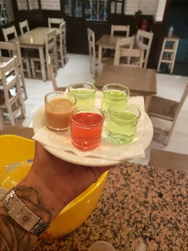 Una persona sostiene una bandeja con cinco chupitos de colores en un restaurante.