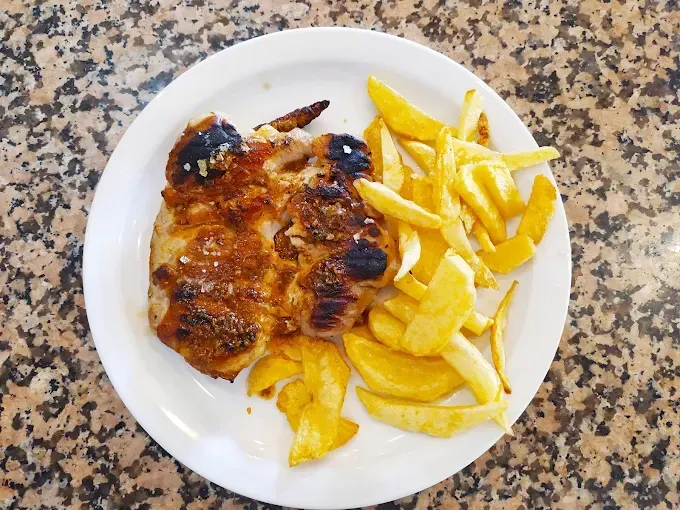 Carne a la parrilla con patatas fritas en un plato blanco.